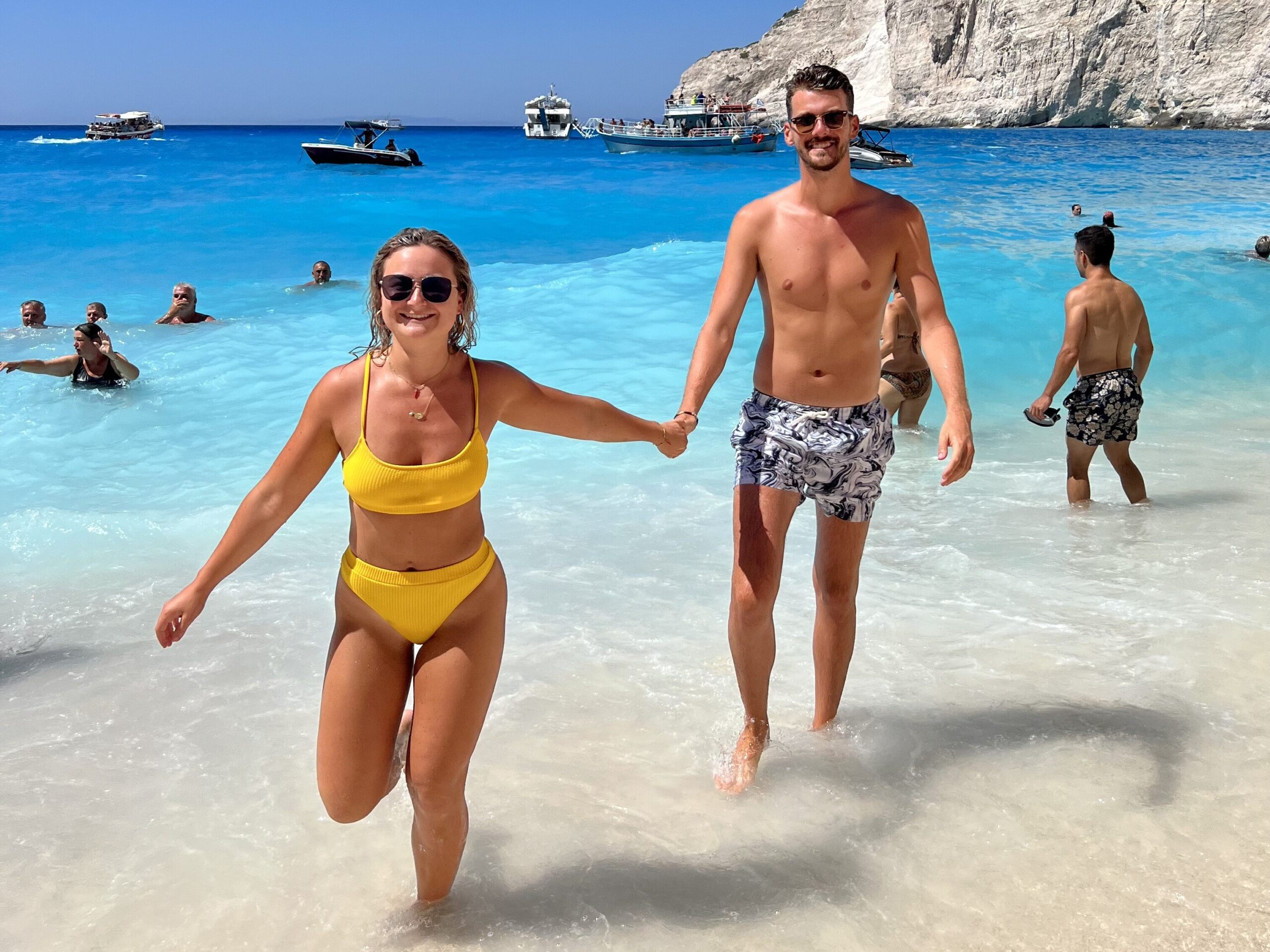 Harry and Renee exploring the Greek islands with turquoise waters and white-washed buildings in the background